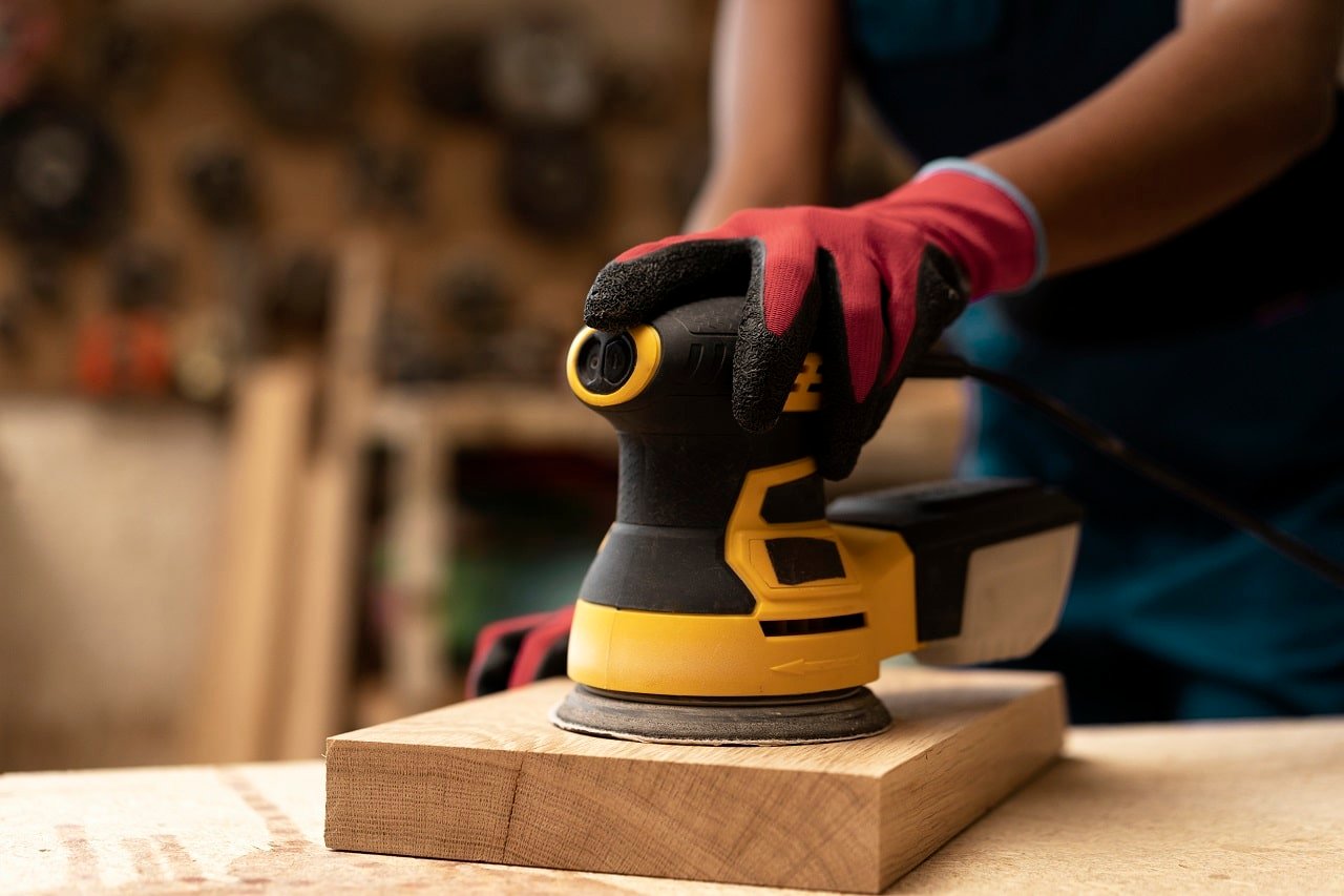 Un homme ponçant une planche de bois avec une ponceuse excentrique électrique