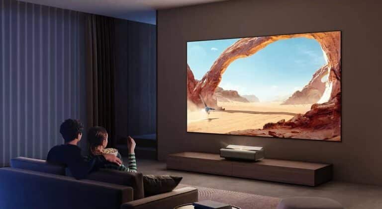 Un jeune couple installé dans un canapé regardant un film projeté sur un un écran géant par le projecteur UTC Xgimi Aura 2