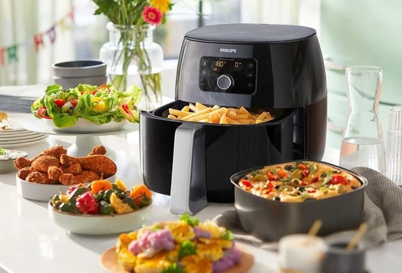 Une friteuse à huile de la marque Philips posée sur un plan de travail. Il y a des plats autour de l'appareil.