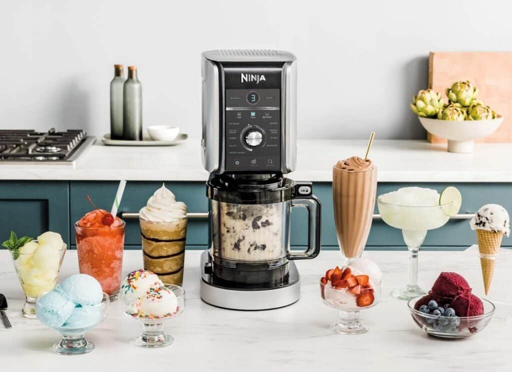 Le Ninja Creami Deluxe sur un plan de travail de cuisine blanc entouré de délicieux desserts glacés