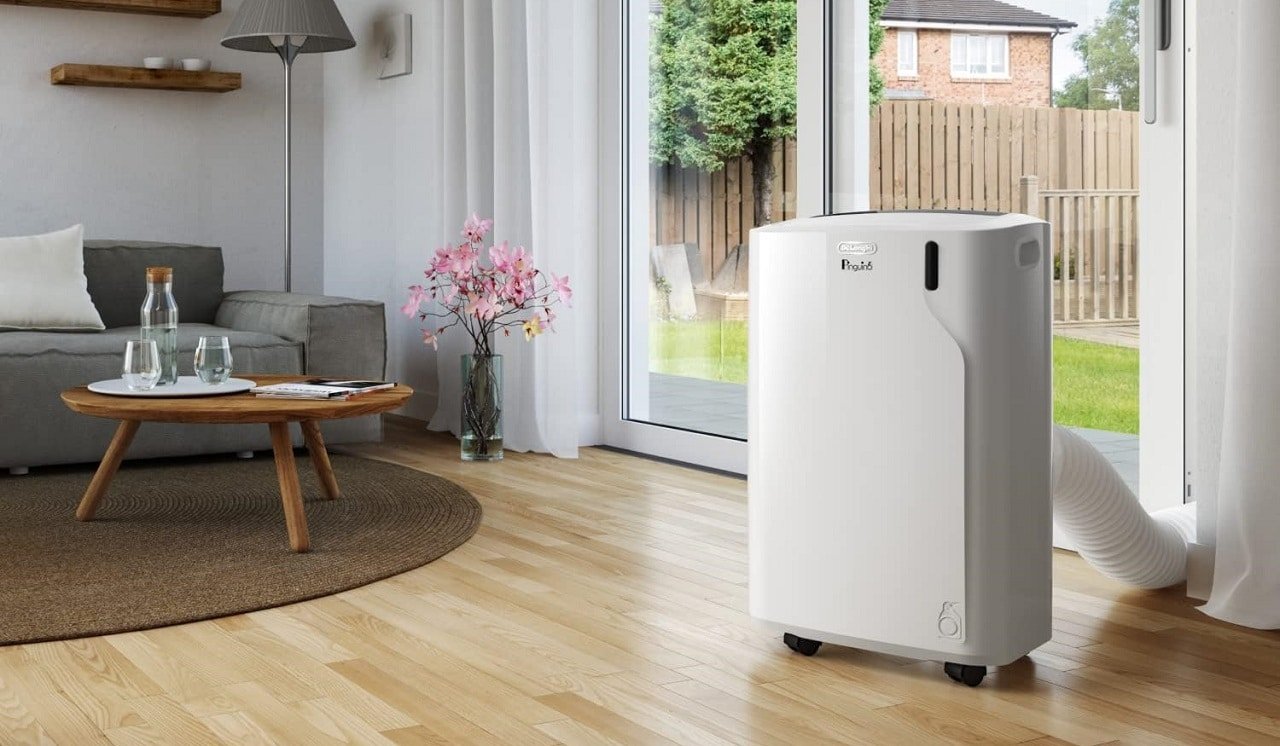 Un climatiseur mobile Delonghi dans un salon devant une baie vitrée et un sol en stratifié