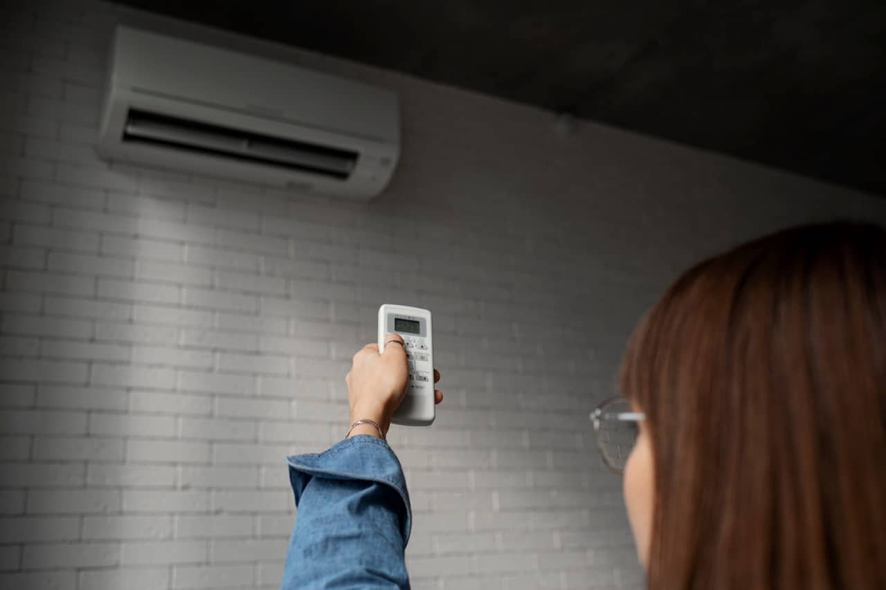 Une femme réglant son climatiseur mural avec la télécommande