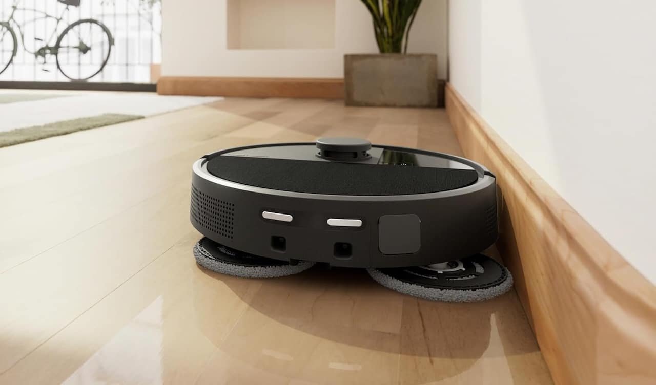 Un robot aspirateur noir de la marque iRobot qui aspire le parquet d'un salon.