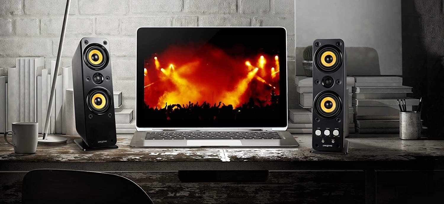 Un PC portable posé sur un bureau avec de chaque coté des enceintes PC de la marque Creative
