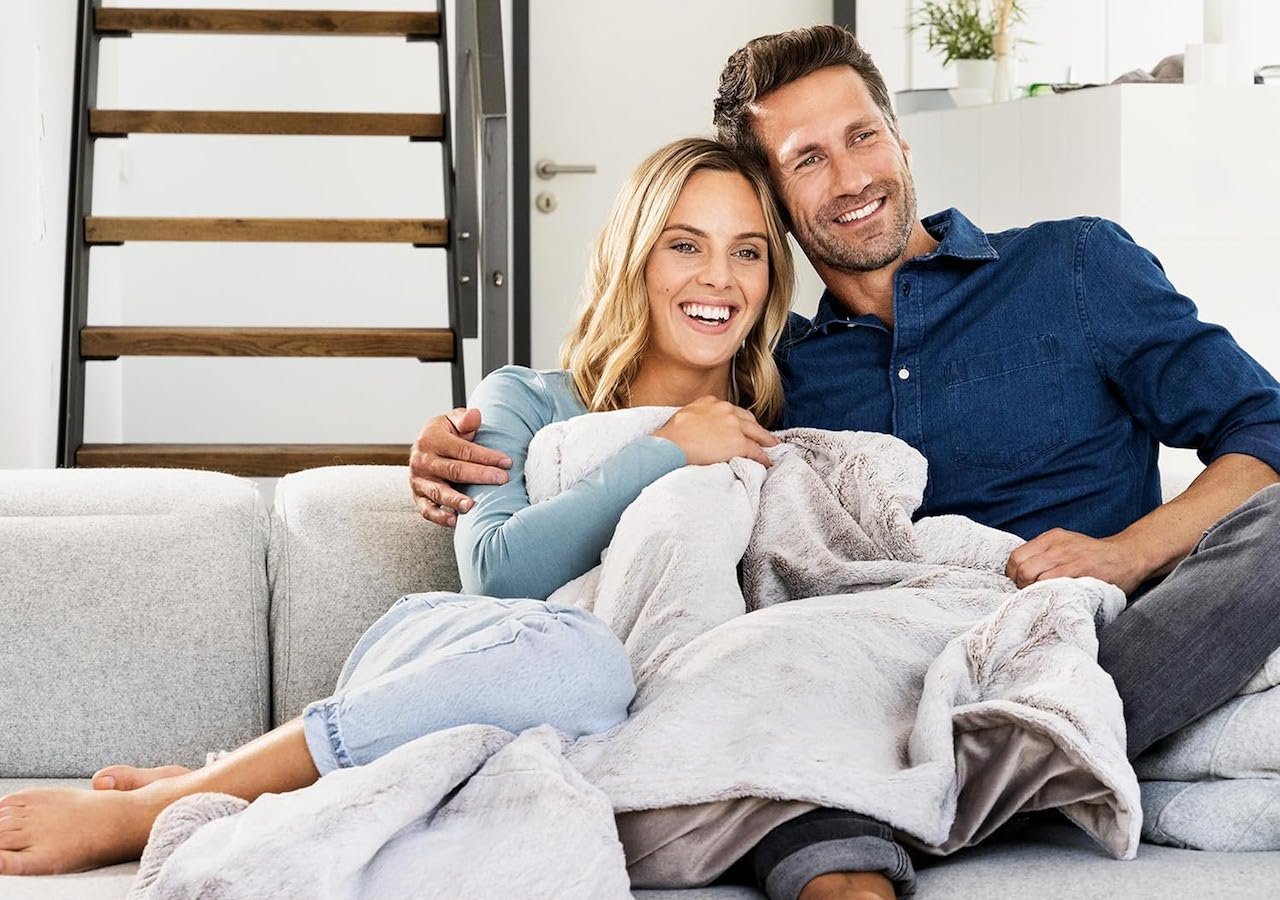 Un couple qui se repose sur leur canapé avec une couverture chauffante.