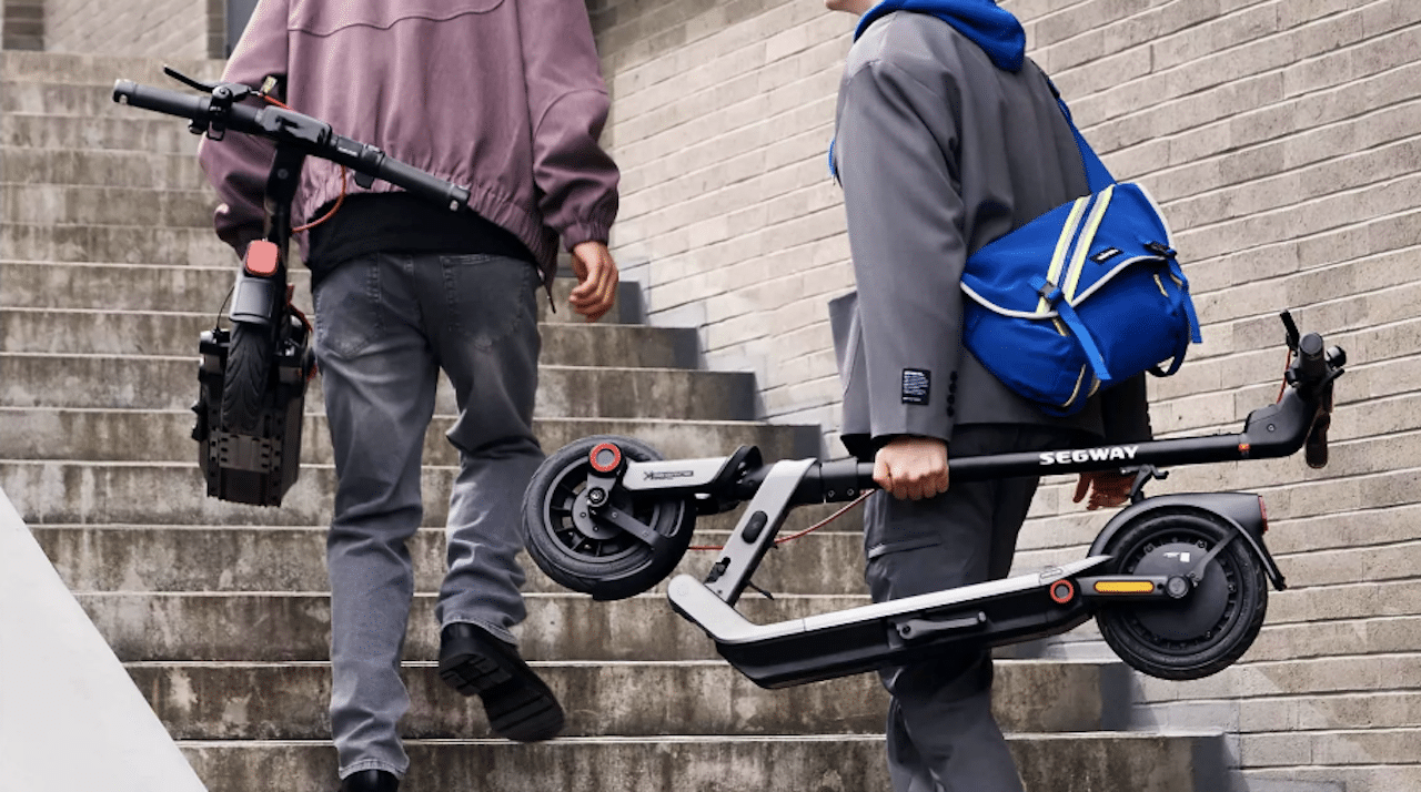 Deux garçons qui portent des trottinettes électriques.