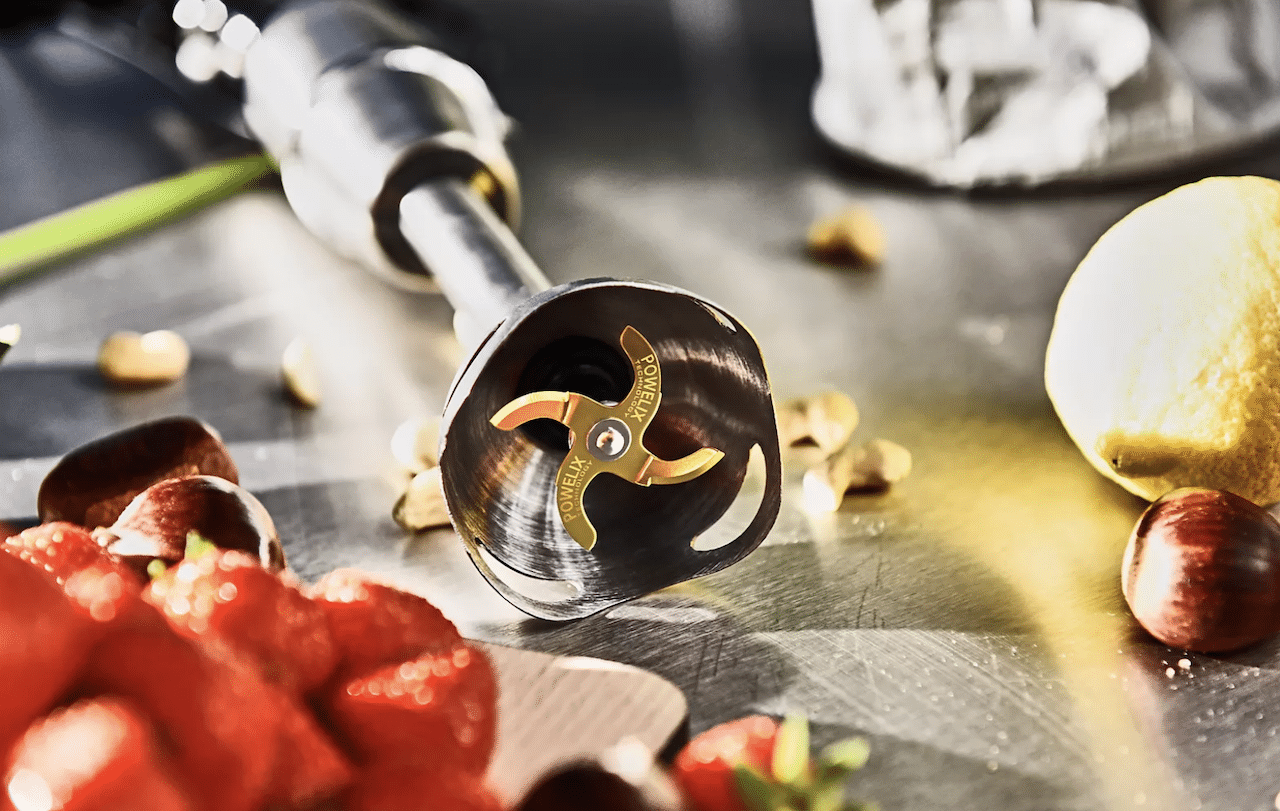 Un mixeur plongeant posé sur une table à côté de légumes.