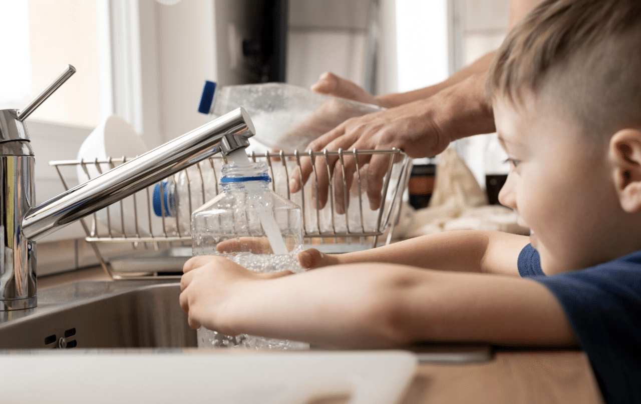 Un petit garçon qui se sert de l'eau dans un verre depuis le robinet de la cuisine.
